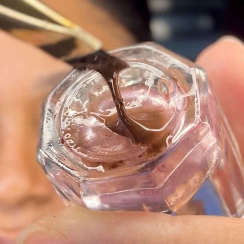 Close-up of brow makeup mixed on glass mixing dish.