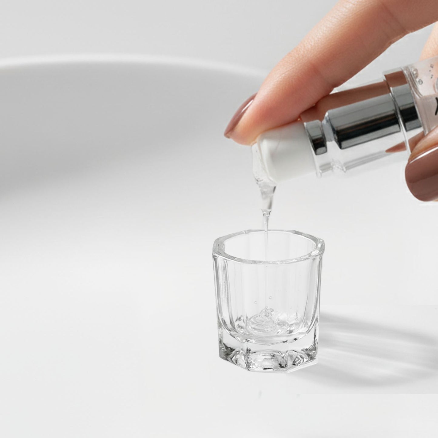 Close-up shot of the Tintology G2 Fuse Activator Gel being pumped from the bottle and dispensed as a clear liquid stream into the small glass mixing dish on a white surface.