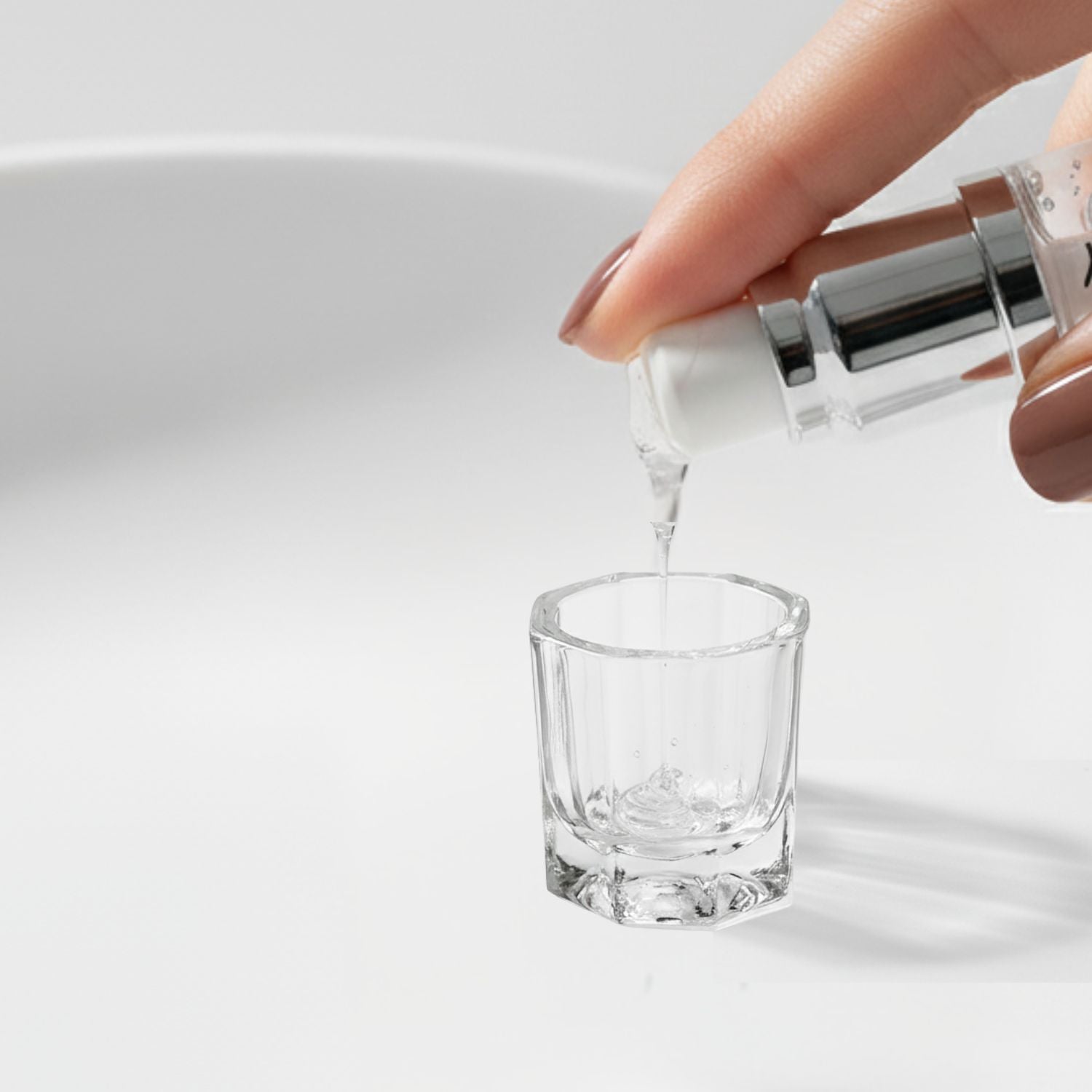 Close-up shot of the Tintology G2 Fuse Activator Gel being pumped from the bottle and dispensed as a clear liquid stream into the small glass mixing dish on a white surface.