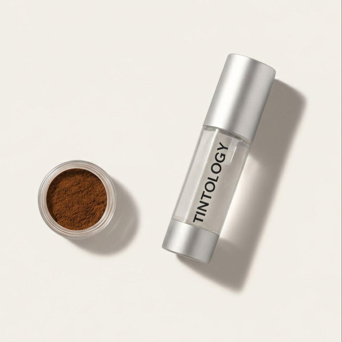 Studio shot of Tintology products: a jar of True Tone Pigment (medium brown powder) next to a bottle of G2 Fuse Activator Gel (clear liquid) with a silver pump dispenser.